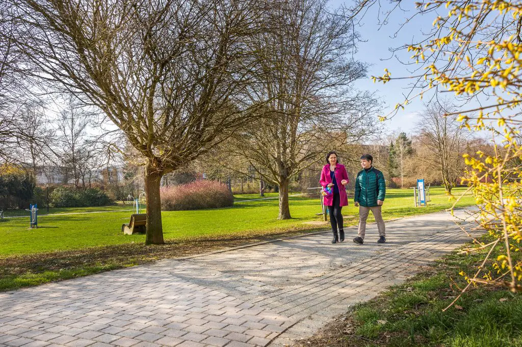 Zwei Personen laufen einen Weg im Park entlang.