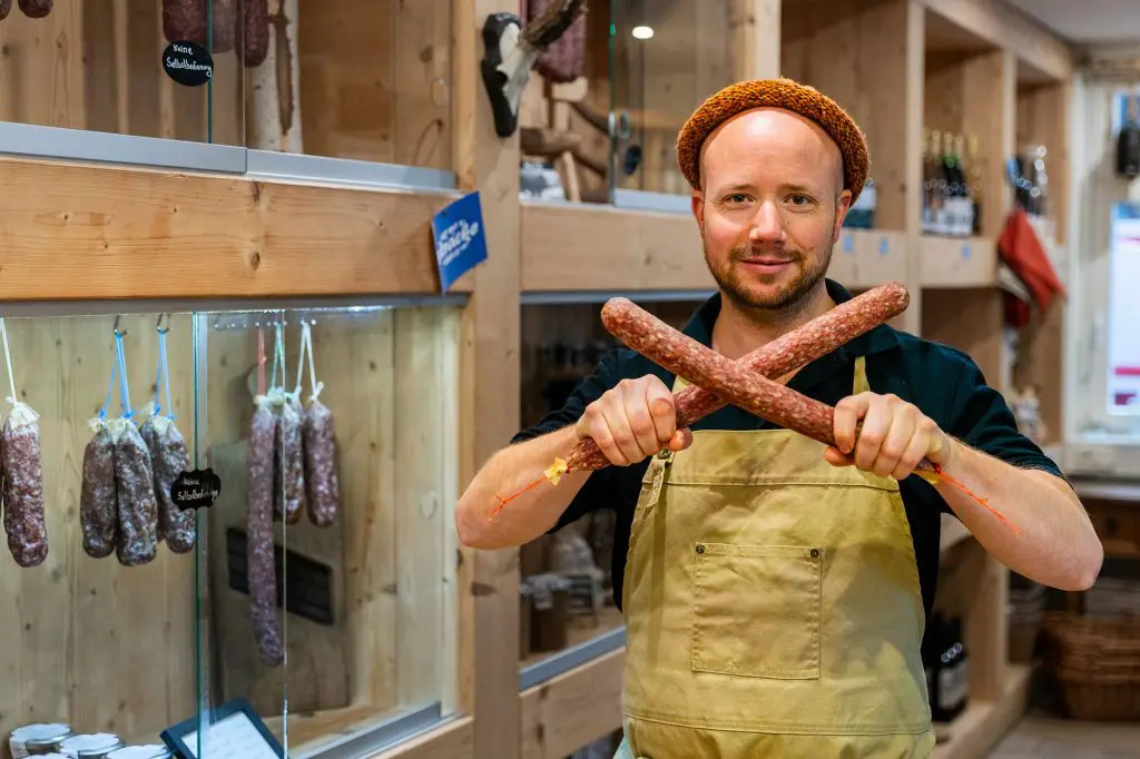 Simon in dem 'Worschtkopp' Hofladen, einem Ort, an dem regionale Produkte und handgemachte Spezialitäten im Mittelpunkt stehen. Mit einem freundlichen Lächeln zeigt er seine Leidenschaft für Qualität und Nachhaltigkeit, die er in seinem Geschäft lebt. Foto: David Heise