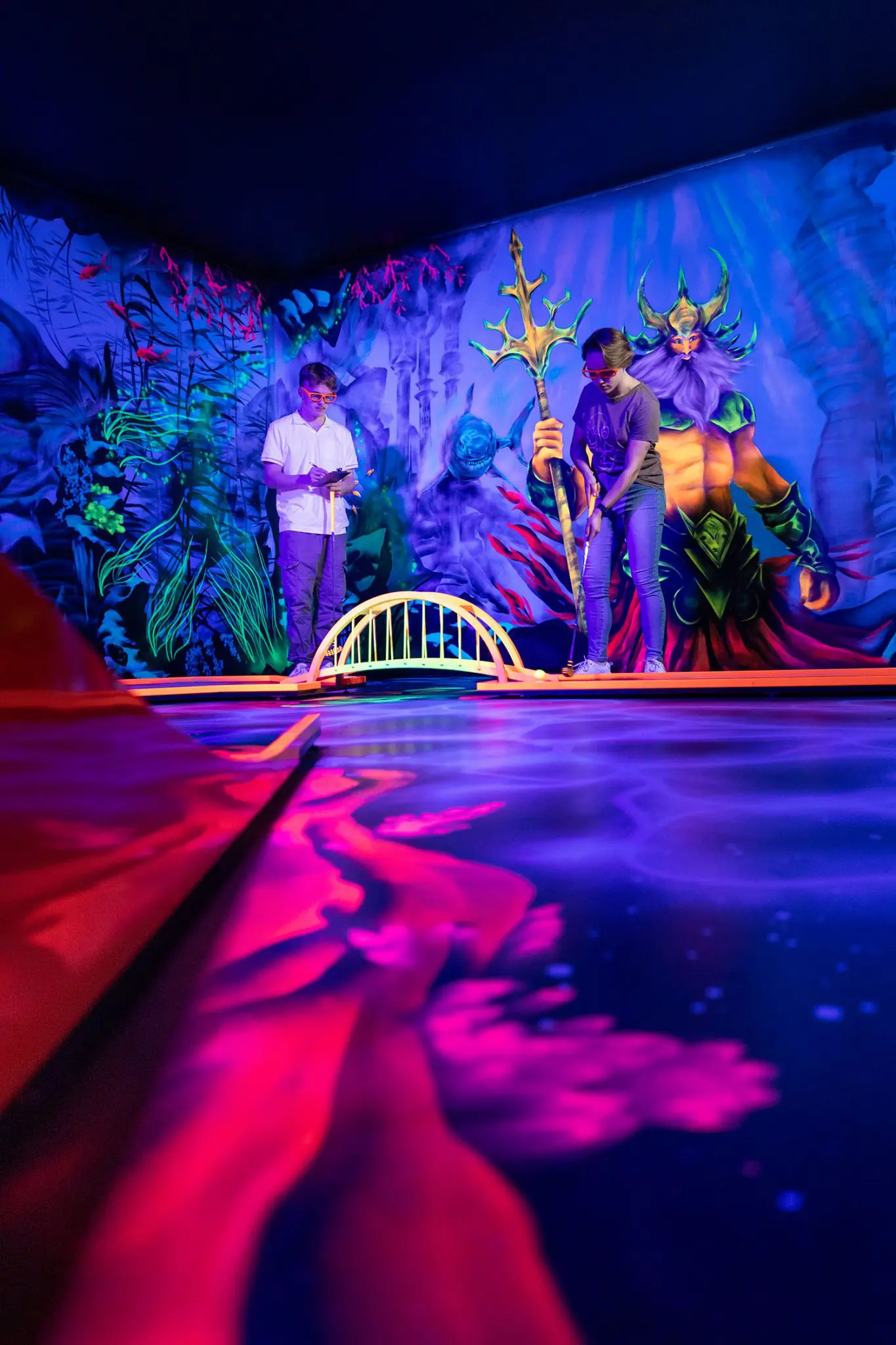 In einer futuristischen 3D-Minigolf-Anlage spielen Laura und Florian begeistert auf einem Parcours, der sie durch verschiedene thematische Welten führt. Umgeben von leuchtenden Graffitis und lebendigen 3D-Effekten, die den Raum in eine Unterwasserlandschaft und eine Dinosaurierwelt verwandeln, setzen sie ihre Schläger ein, während der Boden unter ihren Füßen wie ein dreidimensionales Labyrinth erscheint. Mit 3D-Brillen ausgestattet, erleben sie das Minigolf-Spiel auf eine völlig neue Art, wobei die Grenzen zwischen Realität und Fantasie verschwimmen. Foto: David Heise