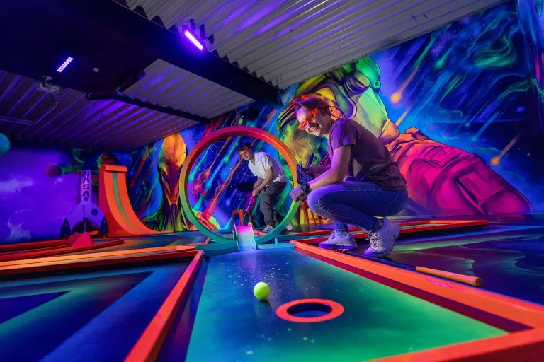 In einer futuristischen 3D-Minigolf-Anlage spielen Laura und Florian begeistert auf einem Parcours, der sie durch verschiedene thematische Welten führt. Umgeben von leuchtenden Graffitis und lebendigen 3D-Effekten, die den Raum in eine Unterwasserlandschaft und eine Dinosaurierwelt verwandeln, setzen sie ihre Schläger ein, während der Boden unter ihren Füßen wie ein dreidimensionales Labyrinth erscheint. Mit 3D-Brillen ausgestattet, erleben sie das Minigolf-Spiel auf eine völlig neue Art, wobei die Grenzen zwischen Realität und Fantasie verschwimmen. Foto: David Heise
