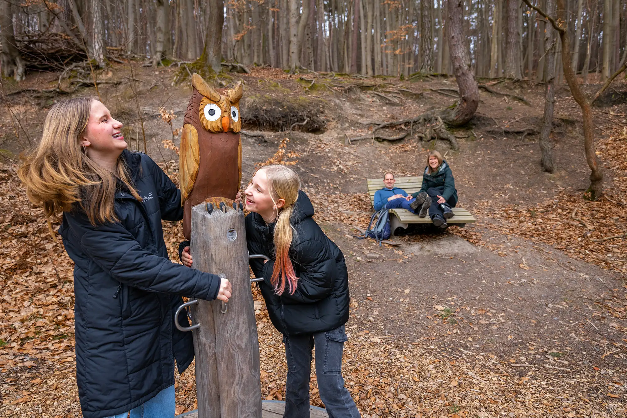 Zwei Kinder spielen mit ihrem Eltern im Hintergrund.