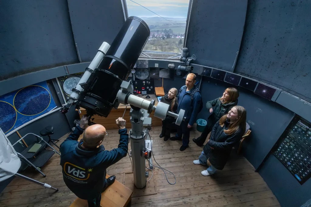 Eine Person zeigt einer Familie die Funktionalität eines Teleskops