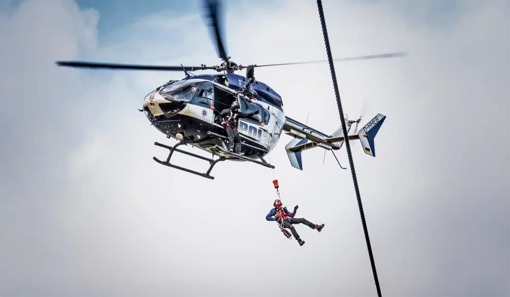 Zwei Bergwacht-Helfer seilen sich aus einem Helikopter ab, fotografiert vom Boden aus.