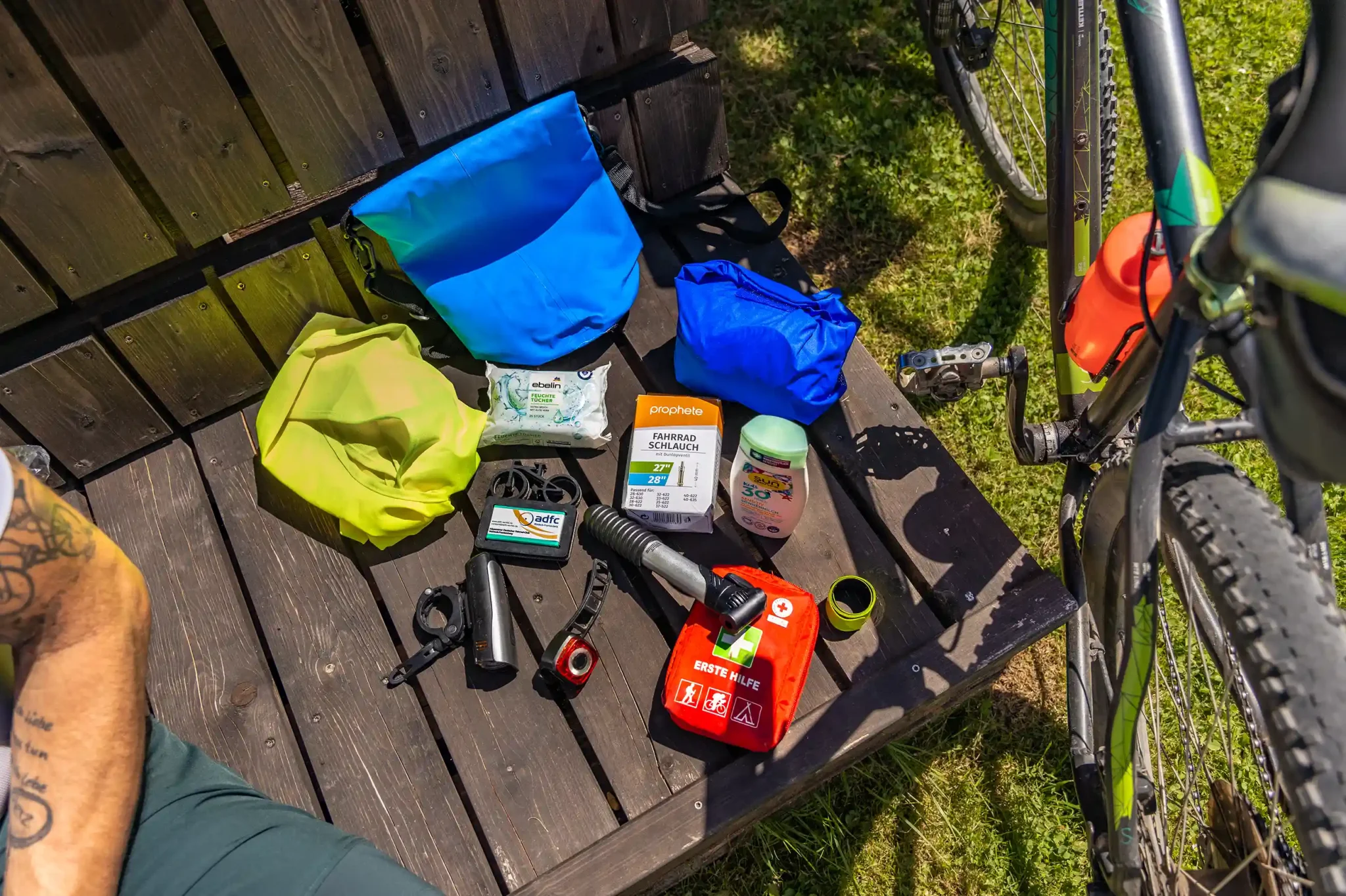 Sammlung wichtiger Fahrrad-Utensilien wie Erste-Hilfe-Kasten, Fahrradpumpe, Sonnencreme und Werkzeug.
