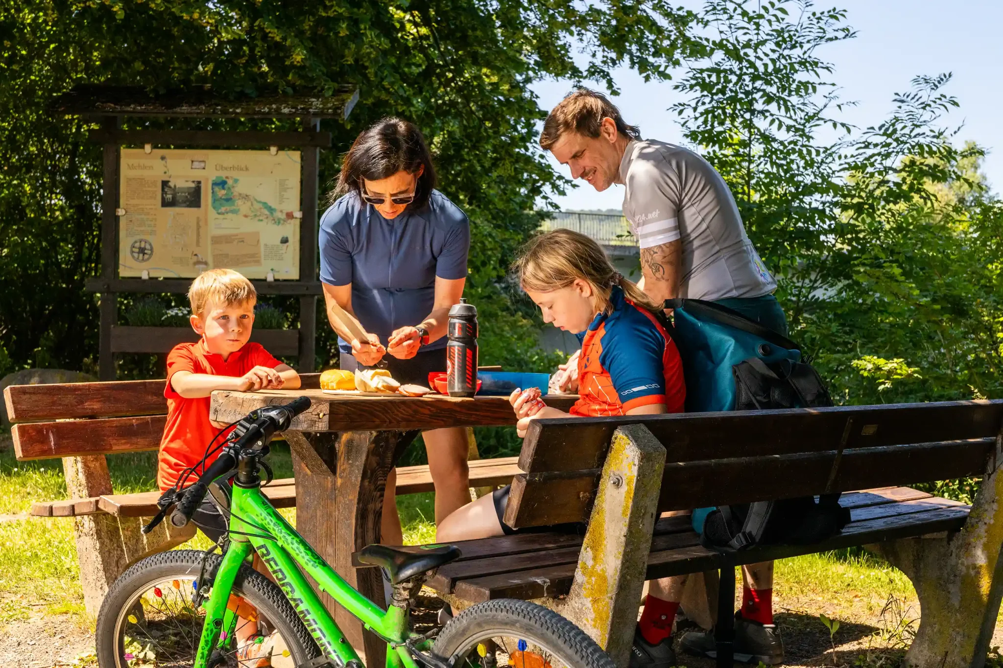 Familie macht eine Essenspause auf einer Bank während einer Fahrradtour in der Natur.