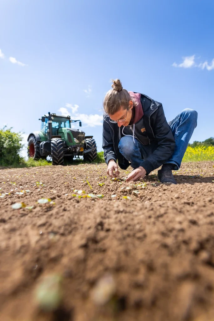 Malte hockt auf dem Feld, im Hintergrund ein Traktor.